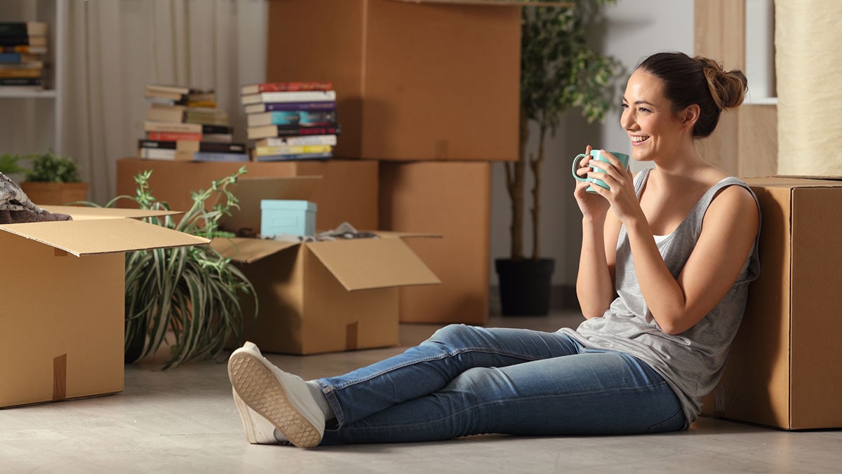 Mujer adulta joven sentada en el piso tomando café con cajas a su alrededor