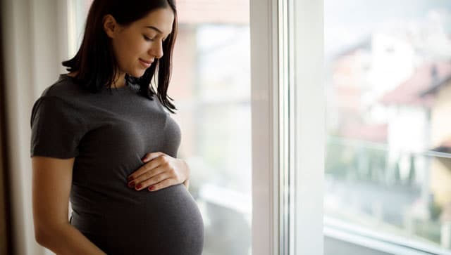 Pregnant woman looks down at her belly.