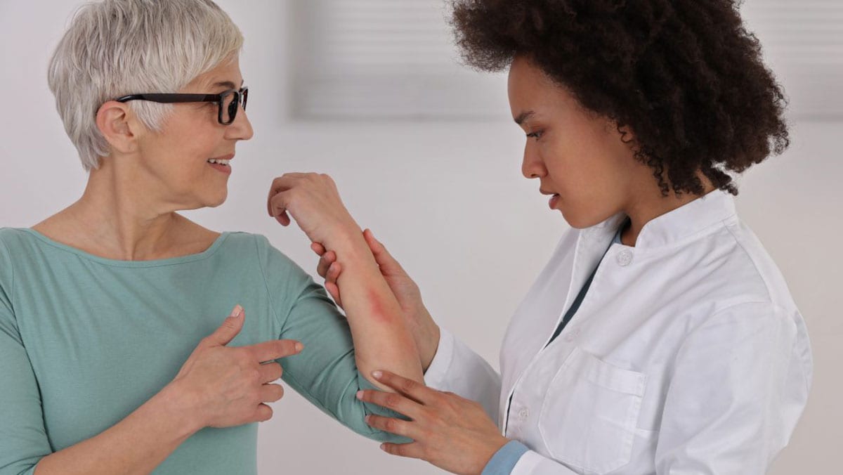 Una mujer mayor con un sarpullido en el brazo es examinada por una dermatóloga.