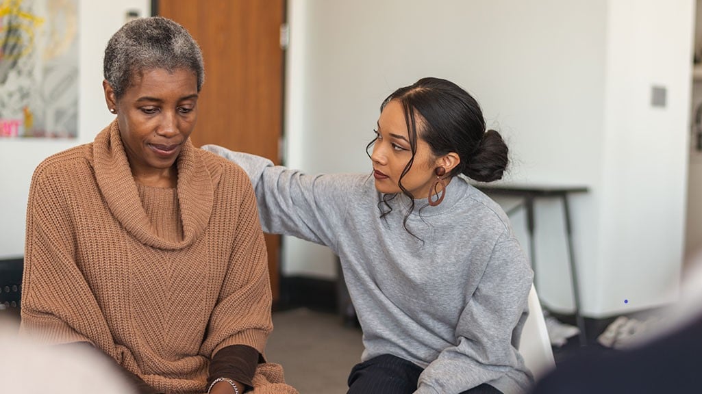 A younger woman comforting an older woman in a group setting