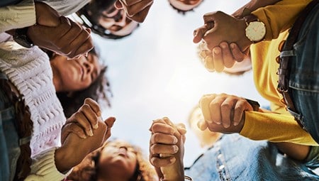 Group of people in a circle holding hands, seen from below