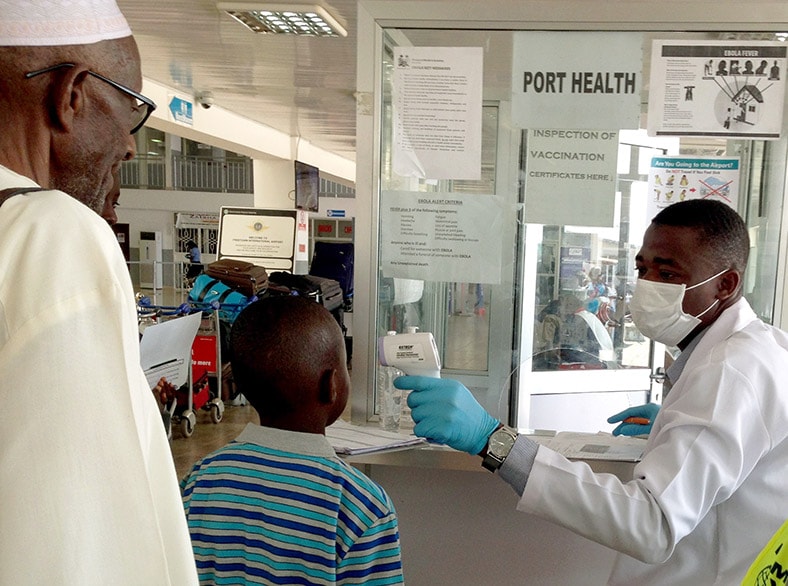 A health worker checks a traveler's temperature to prevent the potential spread of Ebola.