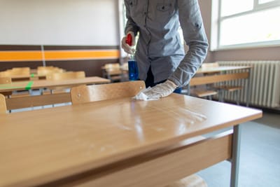 Person wiping down desks with cleaning wipes.