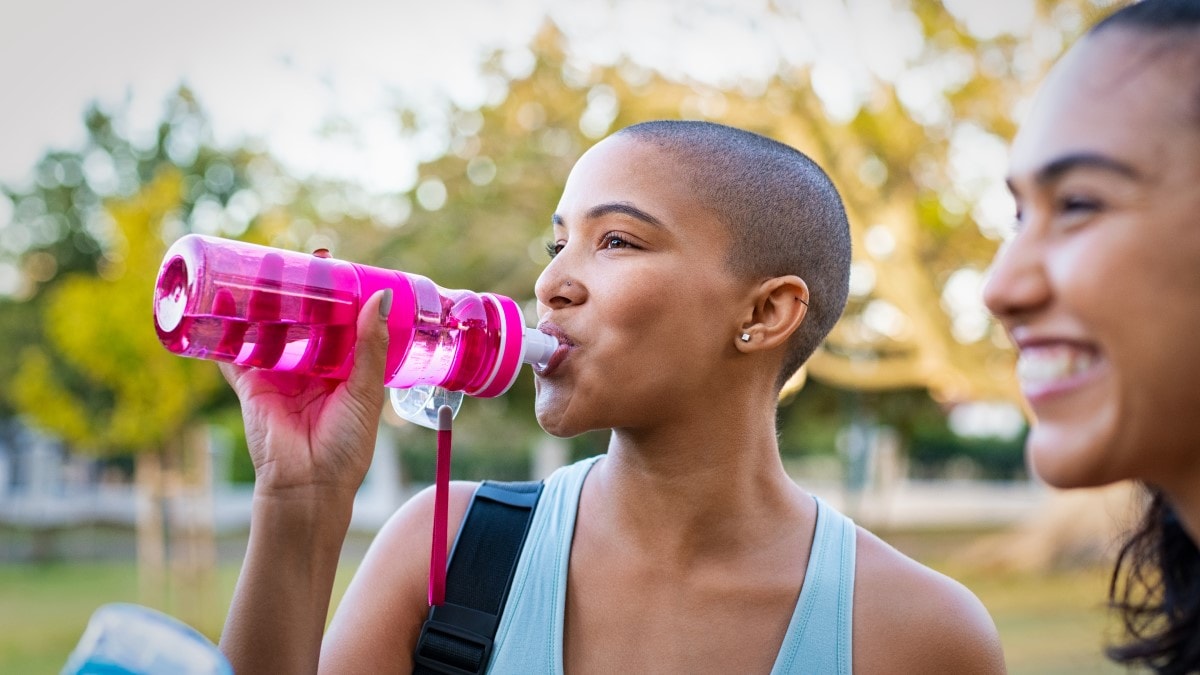 Smiling woman outside drinking water out of a reusable water bottle next to another smiling woman