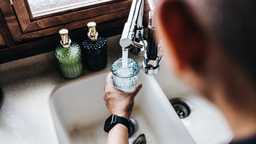 Person filling up a glass with tap water from a kitchen faucet.