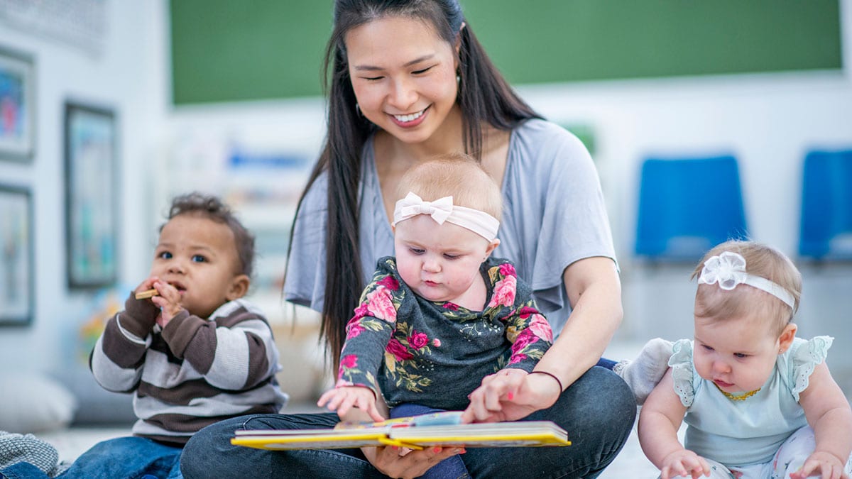 Early care educator sits with three young children