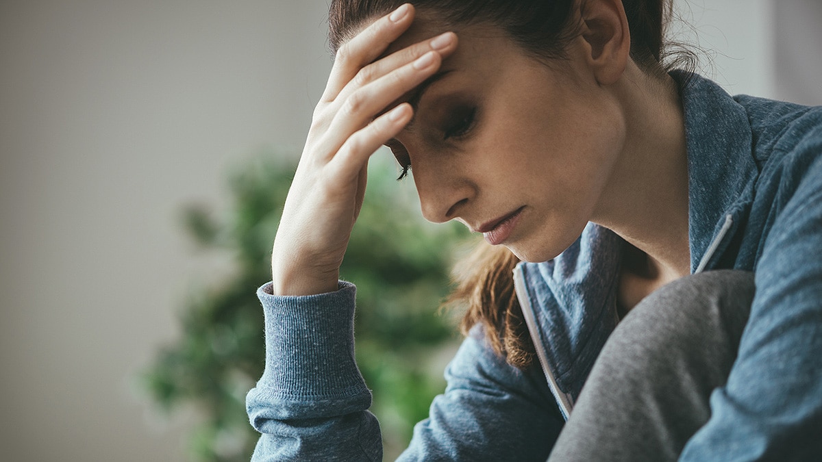 Sad woman bent over holding her forehead in her hand.