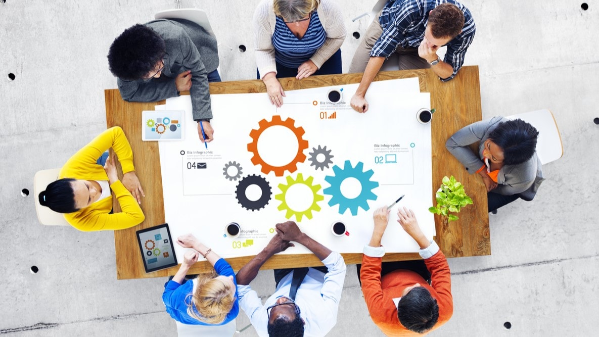 Group of people sitting around a table with graphics of data on a white surface.