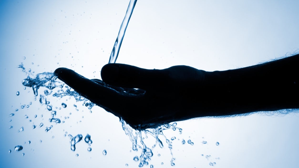 Silhouette of hand with water splashing into it.