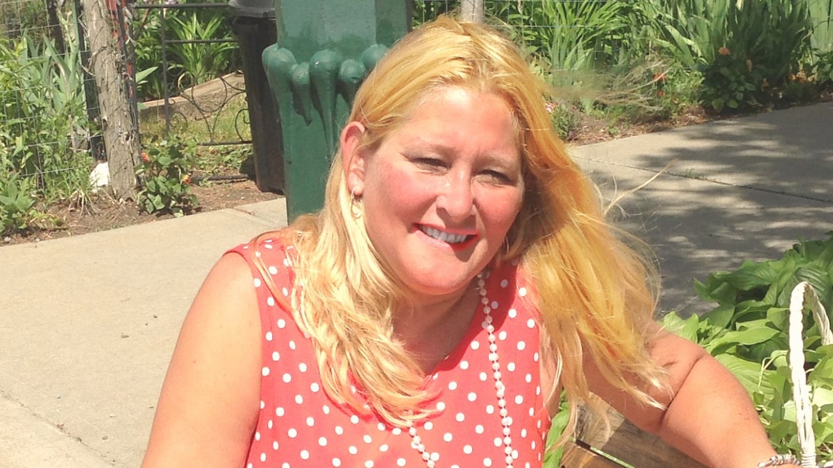 Blonde woman seated outside in park wearing red shirt with white polka dots