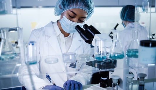 Laboratory workers in lab looking through microscope and writing down findings.