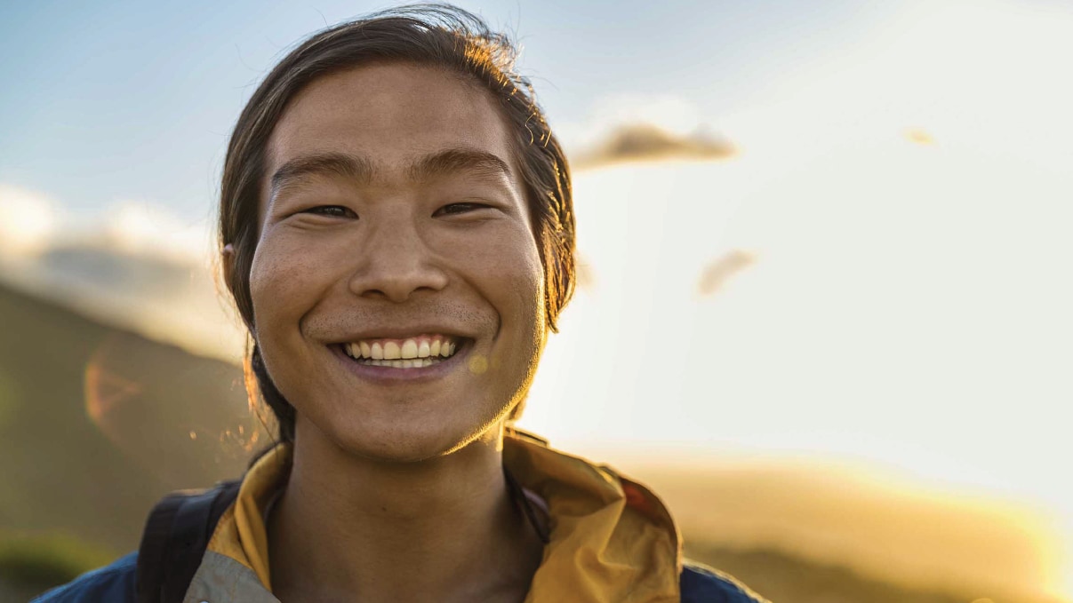 Man smiling outside with mountains in background.