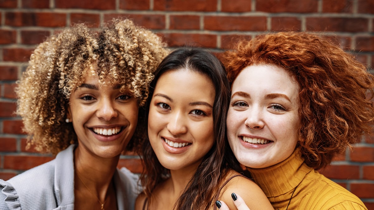 Tres mujeres paradas muy cerca y sonriendo.