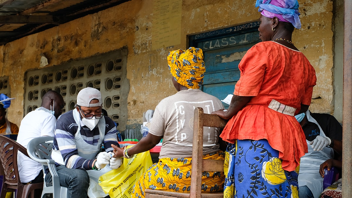 Tech takes fingerstick blood sample from woman while another woman looks on.