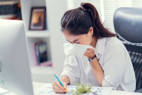 woman at a work desk sneezing into a tissue