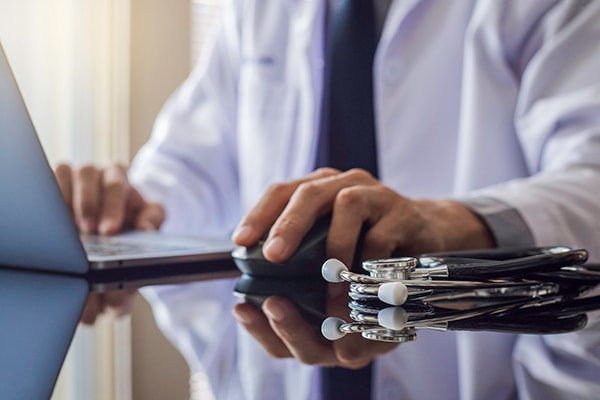 A male doctor working on his computer with stethoscope on the desk.