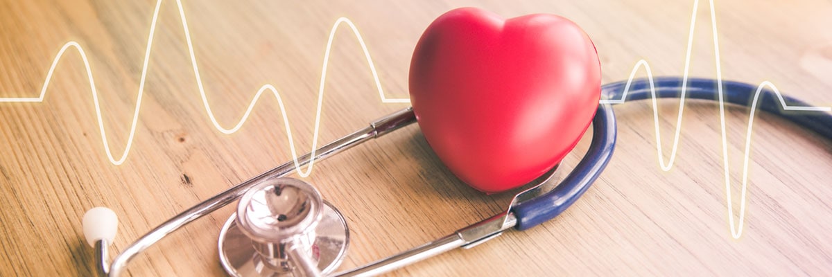 Stethoscope with a red heart and a heartbeat line on a wooden surface, symbolizing heart health.