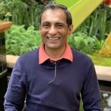 Nimesh Patel is a male with brown hair and brown eyes, smiling at the camera with an outdoor green background.