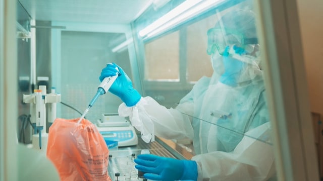 Person in PPE in a lab holding lab equipment.