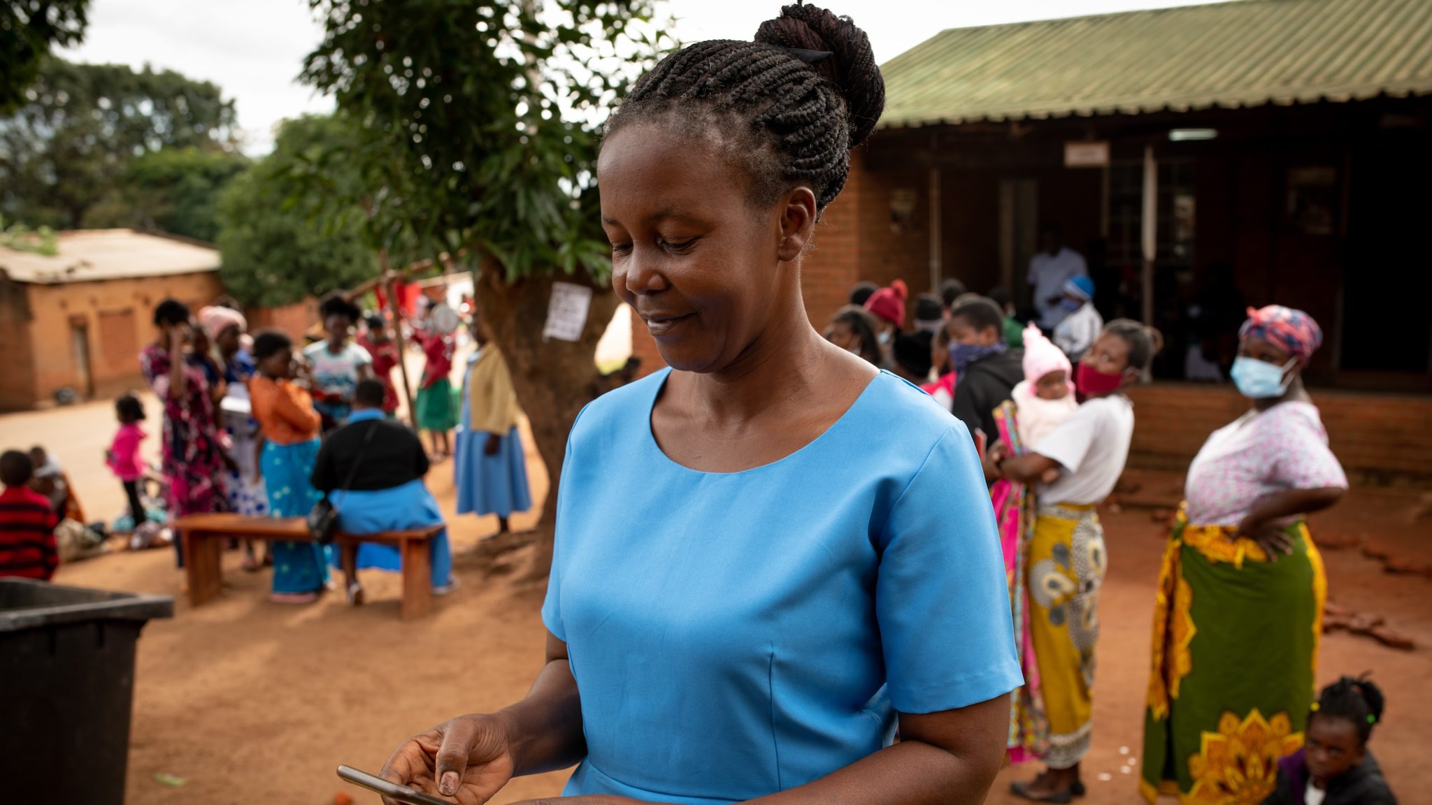 A woman in an African village smiling looking down at a phone.