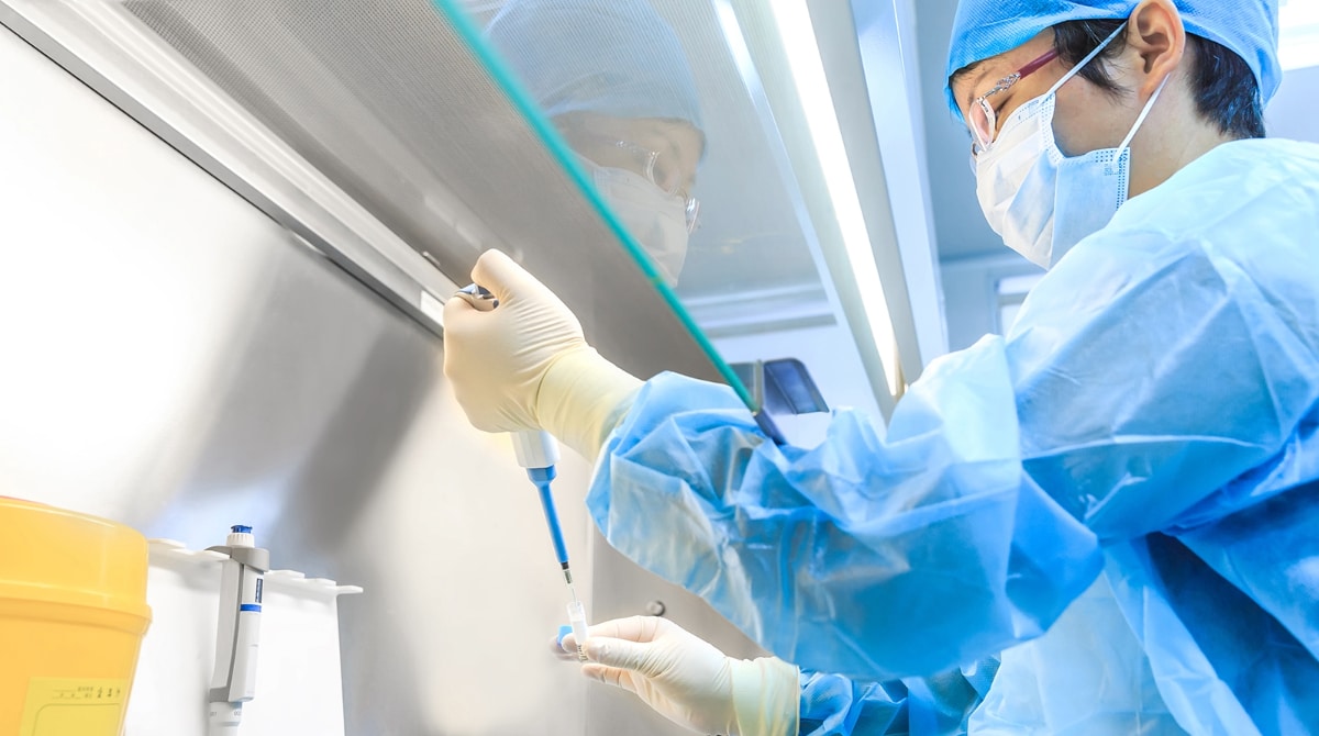 Scientist with personal protective equipment at a laboratory using a pipette.