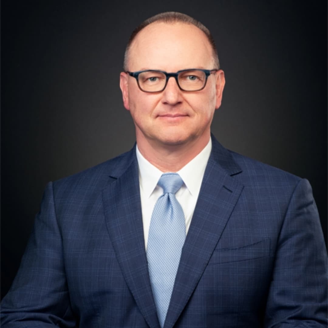 White man with glasses and blue suit and tie smiling.