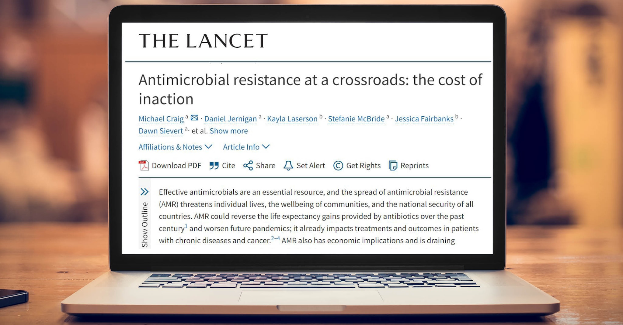 A laptop screen displays an article from The Lancet journal titled "Antimicrobial resistance at a crossroads: the cost of inaction."