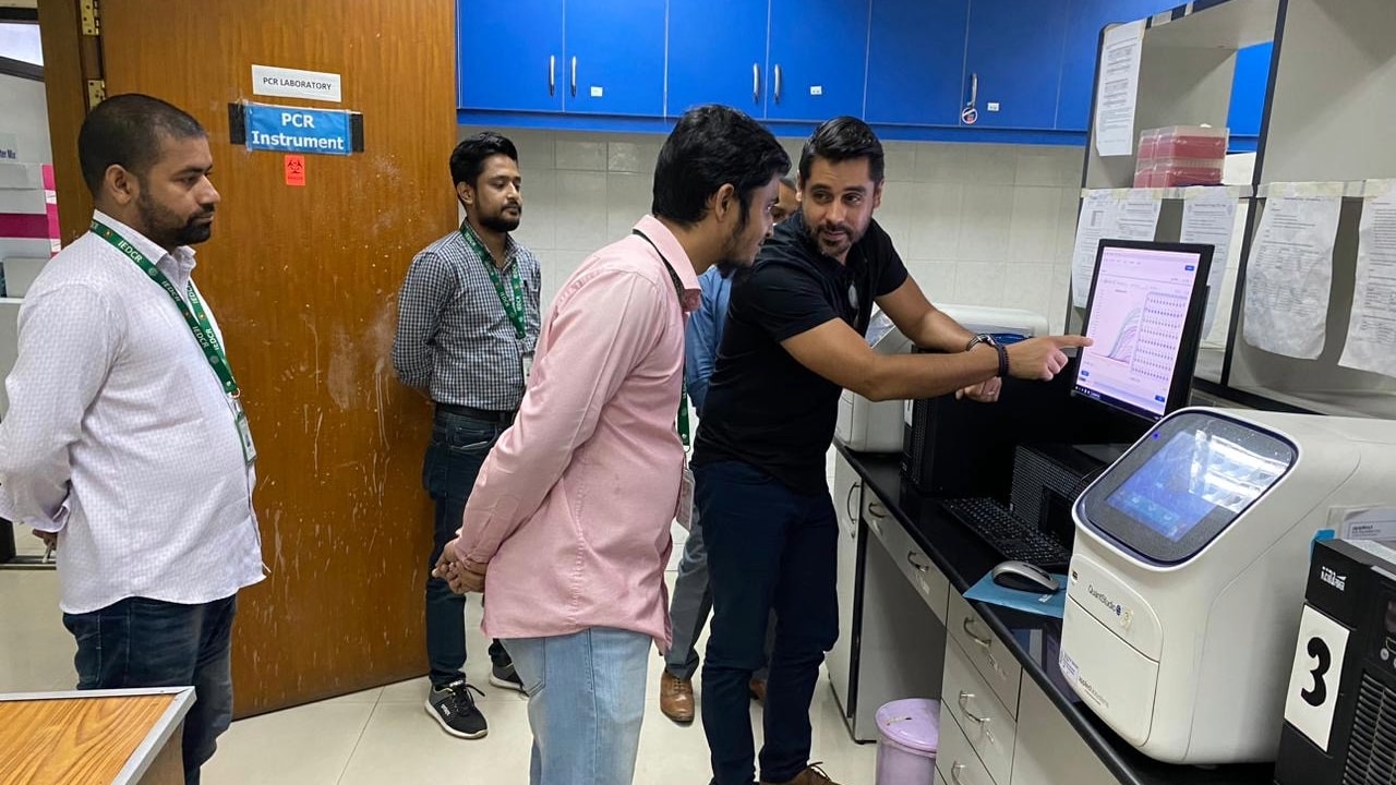 Group of people stand in a room while two look at a computer screen.