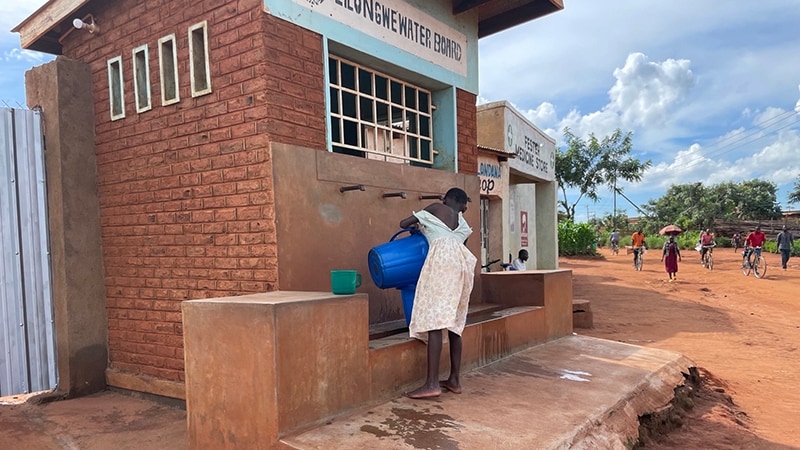 A person holds a bucket while standing in front of an outdoor water station