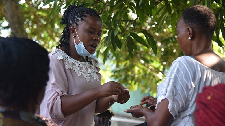 A person hands something to another person during an outdoor village assembly in DRC