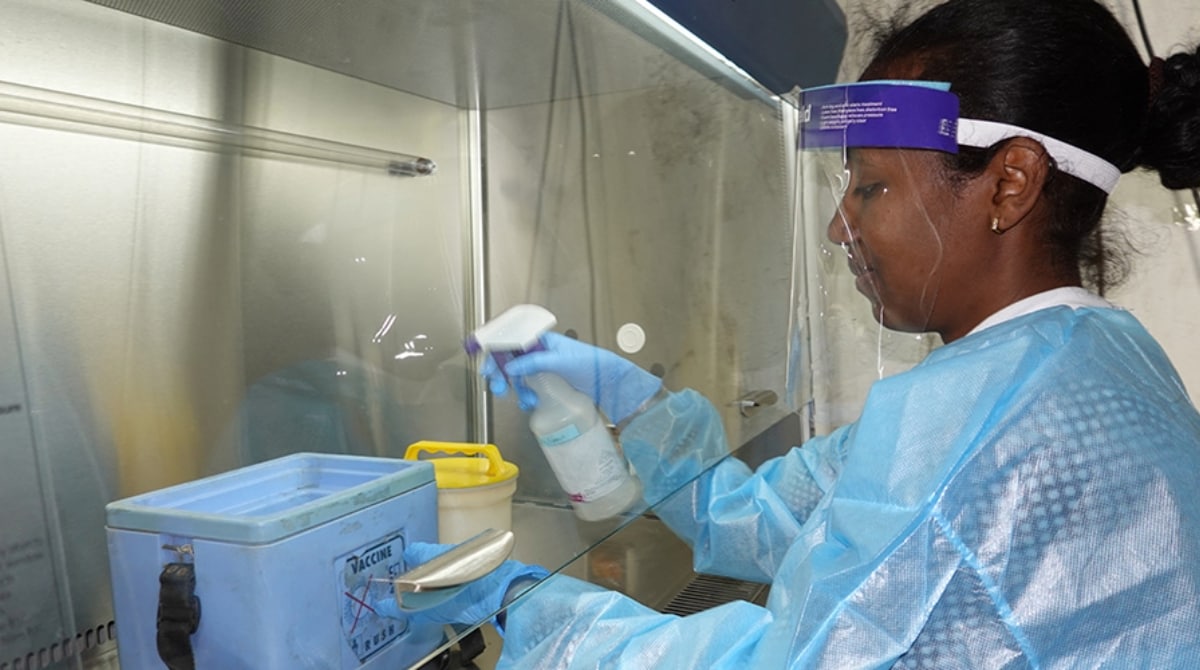 Woman lab worker dressed in personal protective equipment sprays a container in a laboratory setting.