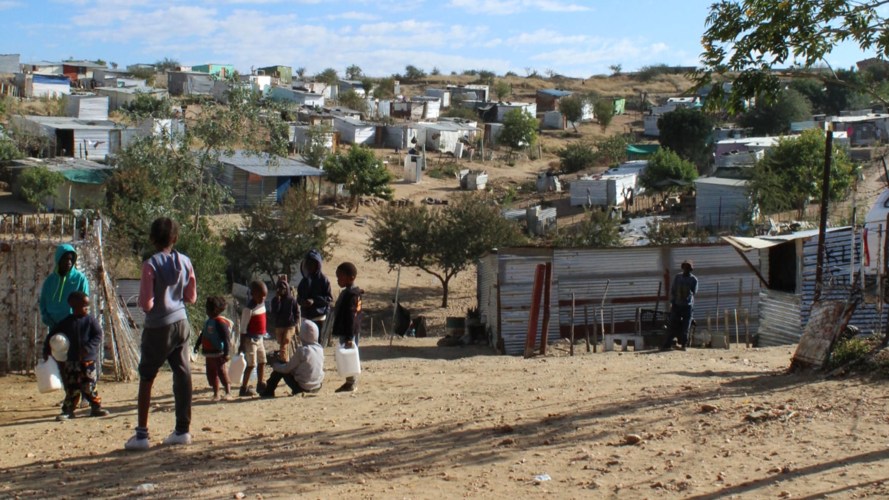 Group of children stand outside on a hilly road. Houses are in the background