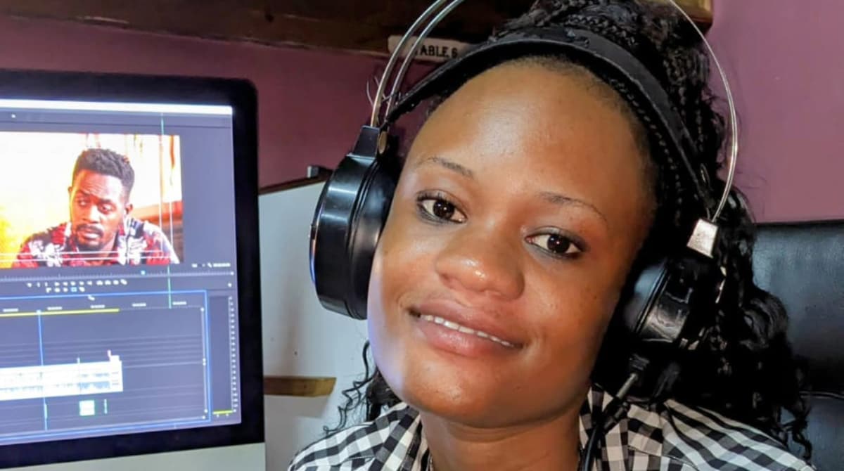 A woman wearing headphones sits in front of a computer screen that is displaying video editing software.