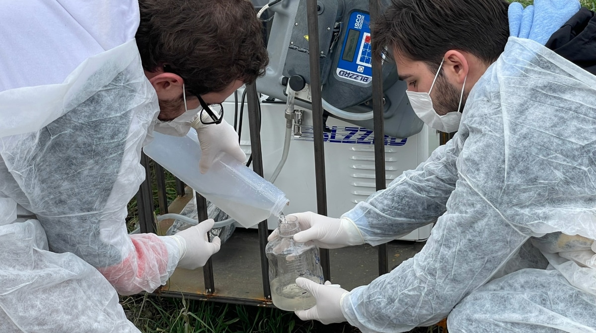 Two workers wearing personal protective equipment and taking a wastewater collection sample.