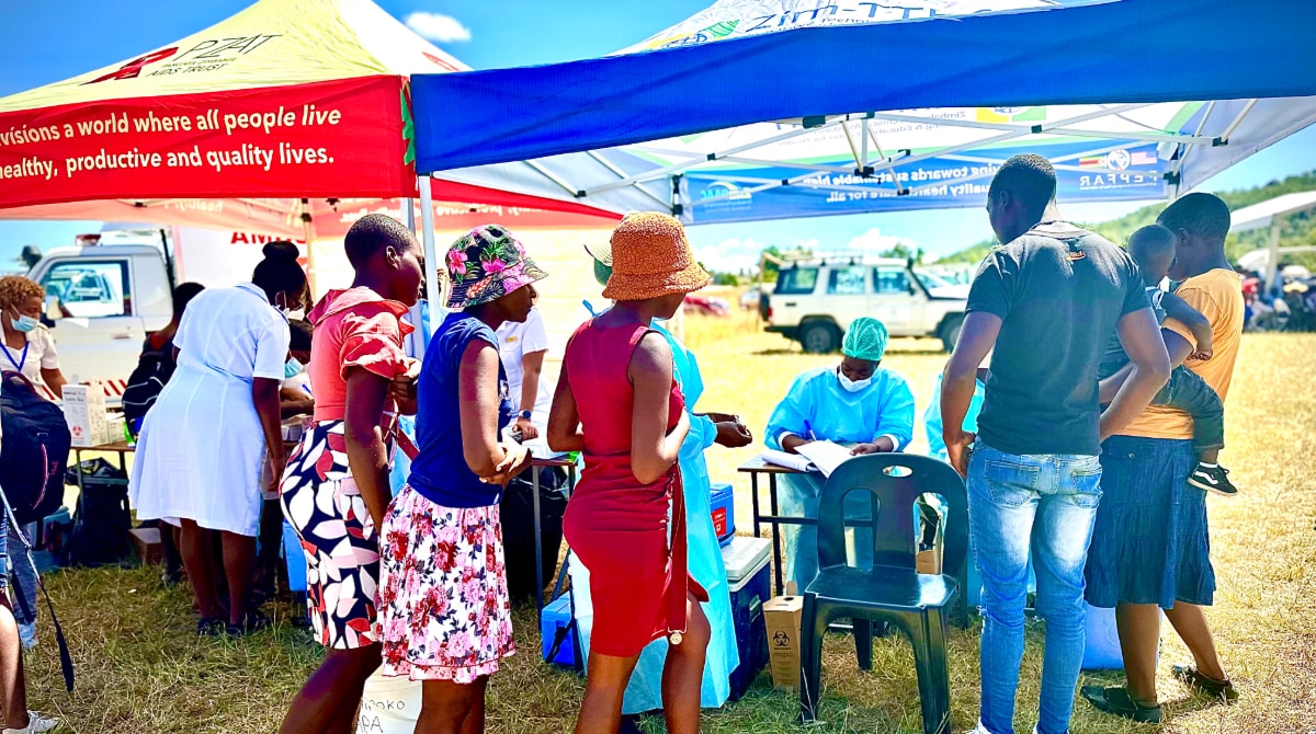 Group of 3 women and and family and baby stand under an outside tent while healthcare worker fills out paperwork.