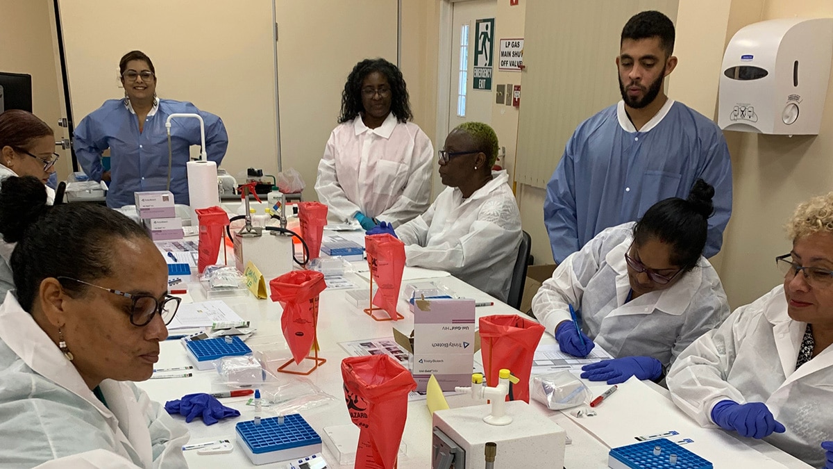 People work around a table with laboratory equipment in front of them.