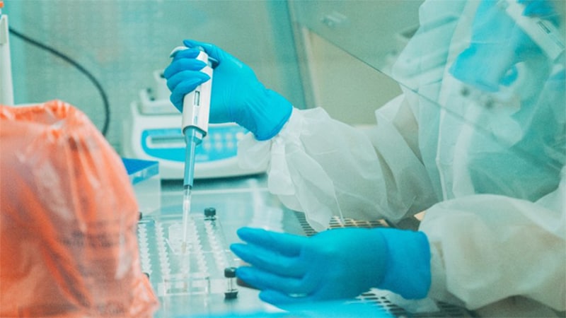 Photo of a laboratorian holding a pipette while wearing gloves and personal protective equipment.