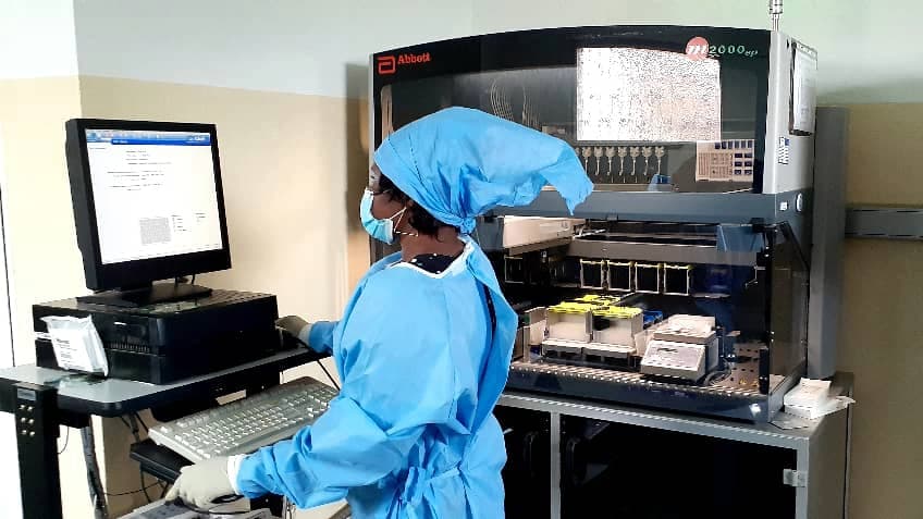 A laboratorian wearing personal protective equipment stands while using a computer.