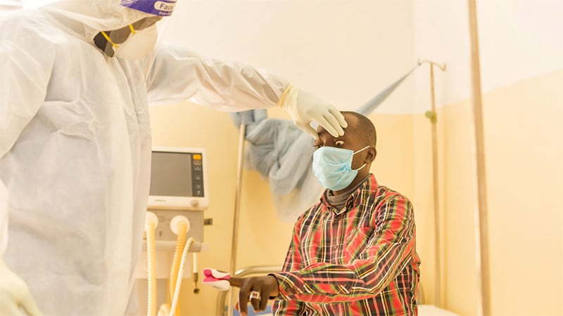 Health worker dressed in full protective gear conducts a health check on a man wearing a mask.