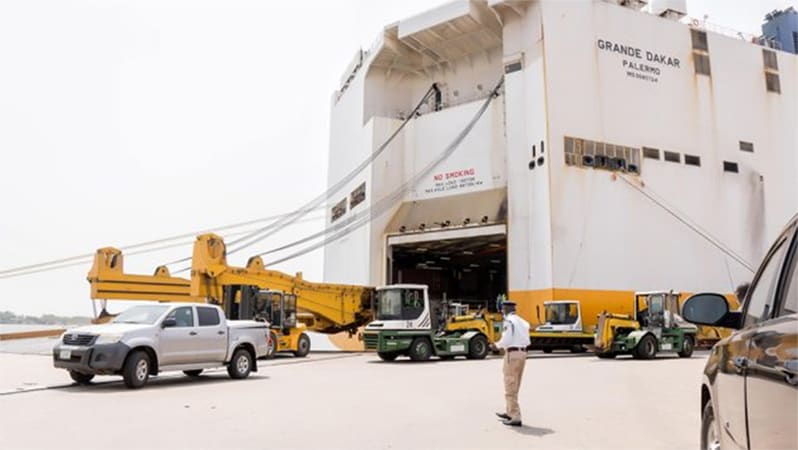 Image of cargo ship surrounding by trucks and Port worker monitoring