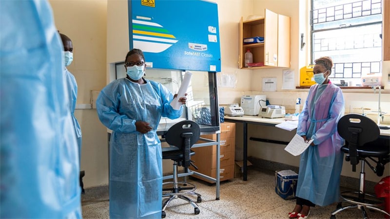 People in protective public health gear talking in a lab