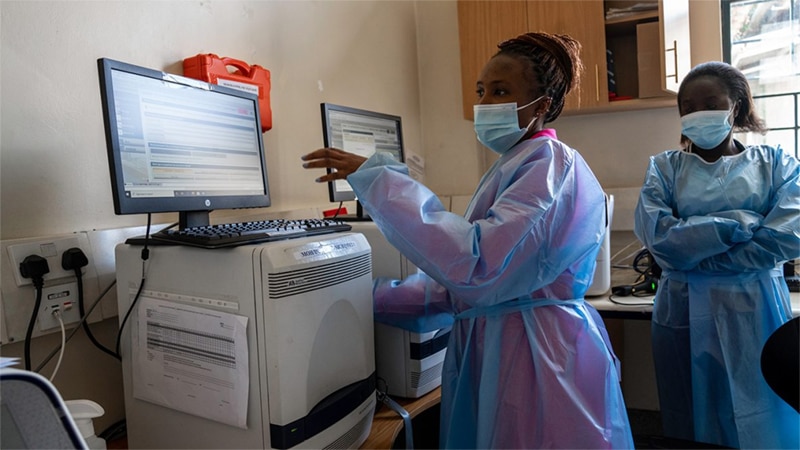 woman wearing mask and protective covering looking at a computer screen