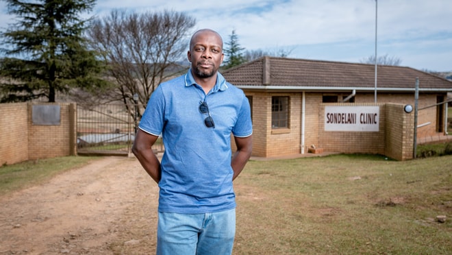 Chimatira is standing in front of a clinic under an open clear sky