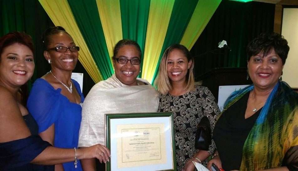 Five women stand in front of a colorful background, holding a certificate.