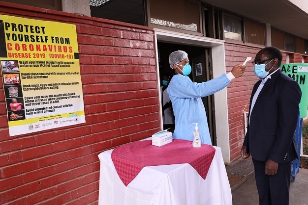 A health care worker takes the forehead temperature of a man outside of a clinic.