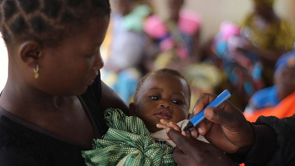 A mother holds her child, whose finger is being marked to show that the child received a polio vaccine.