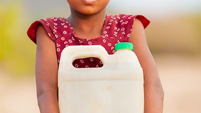 Young girl holding a plastic jug of water outside.