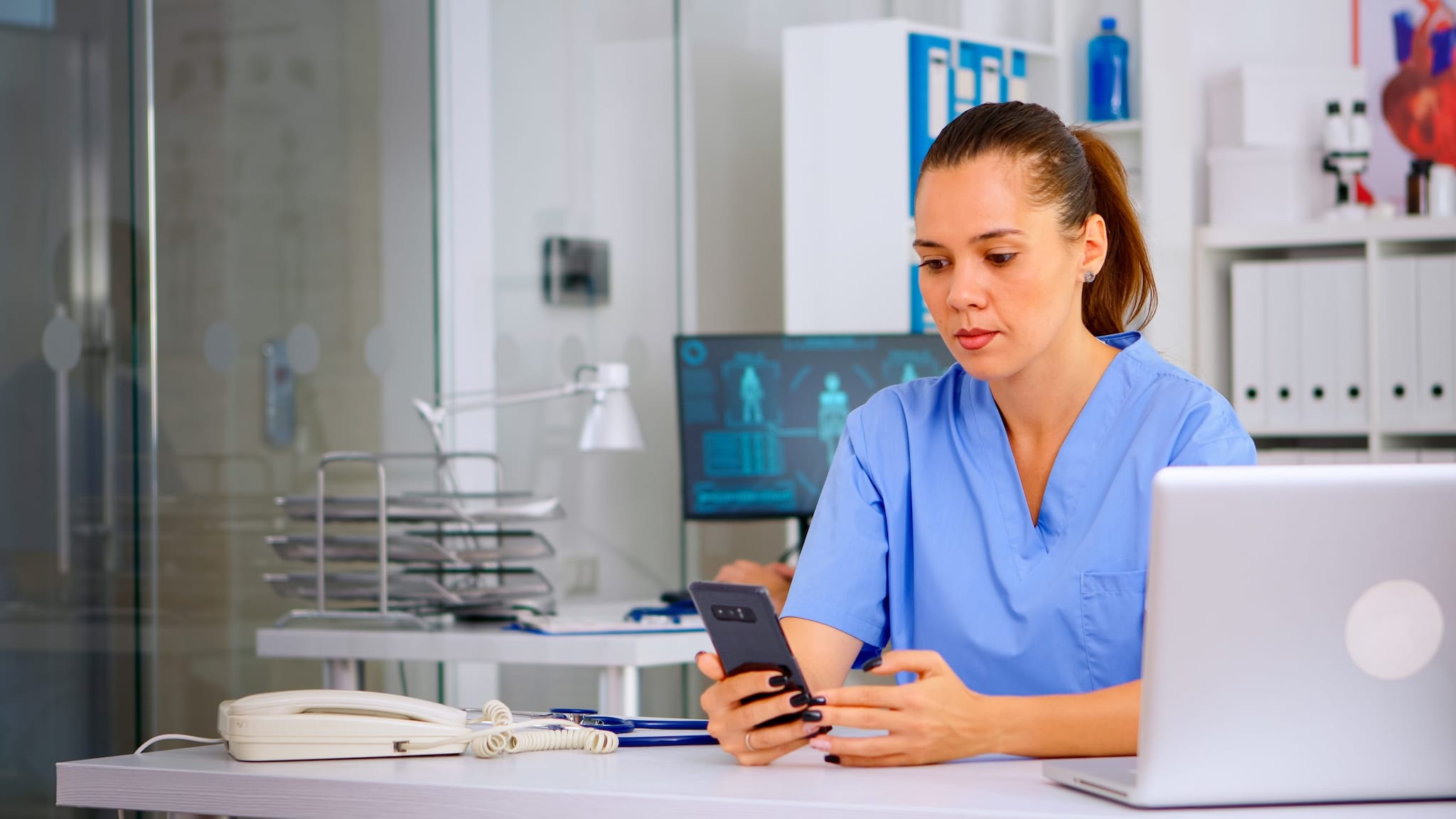 Medical professional sitting at a desk with a computer and a hand-held device.