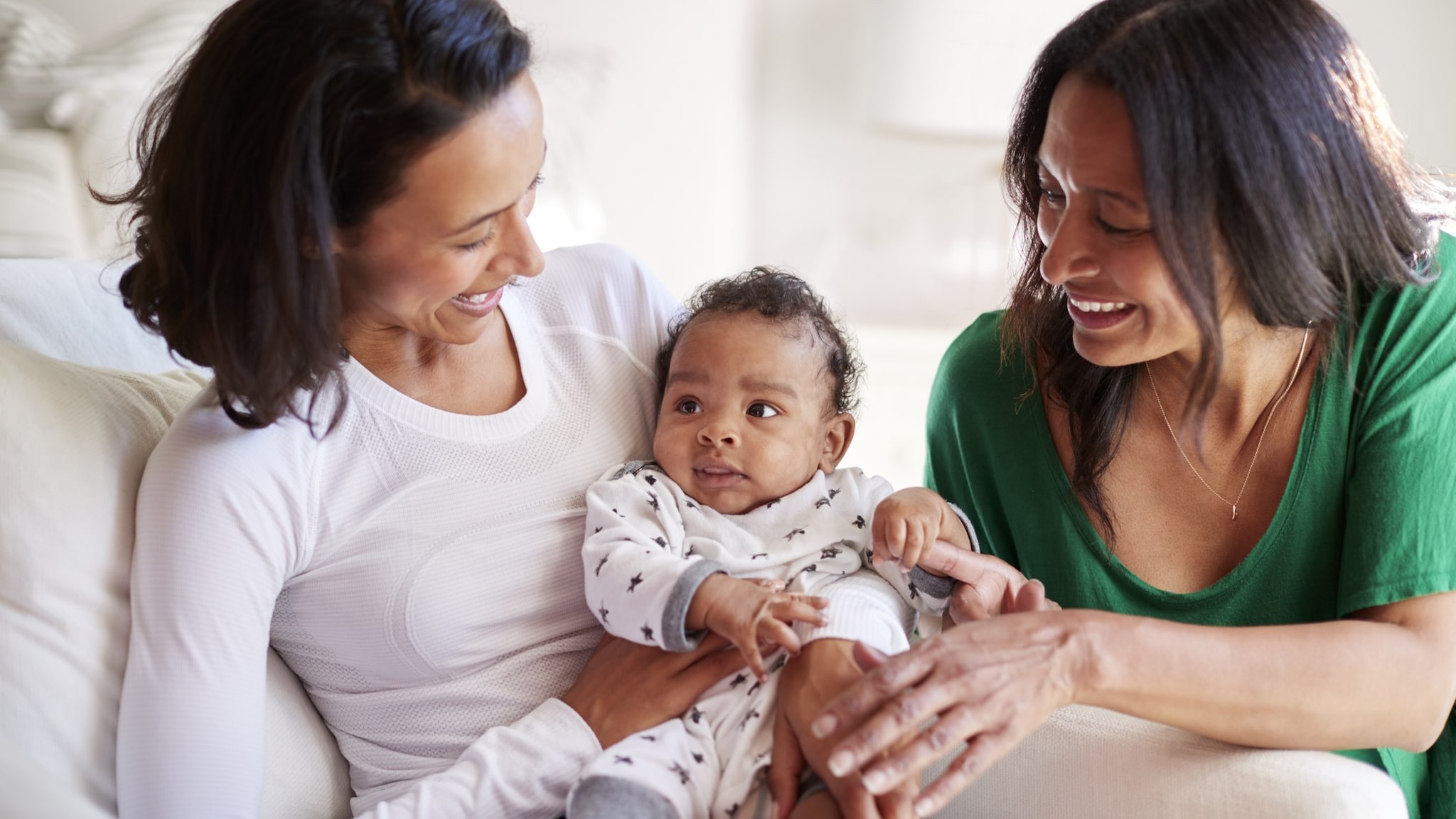 Mother holding an infant while grandmother looks on.