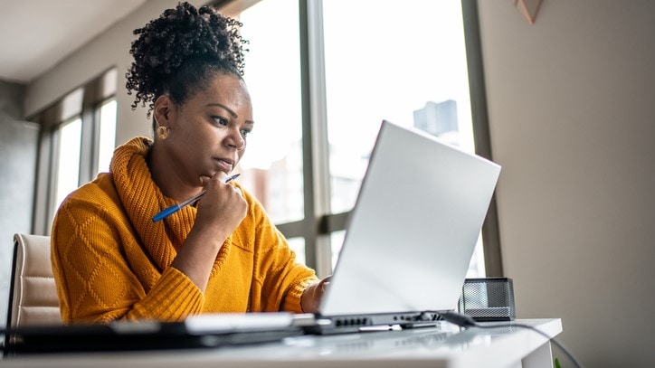 Woman studying a computer screen with a pen in her hand.